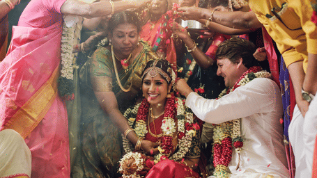 A traditional Indian wedding scene with the bride and groom surrounded by vibrant colours and floral decorations.