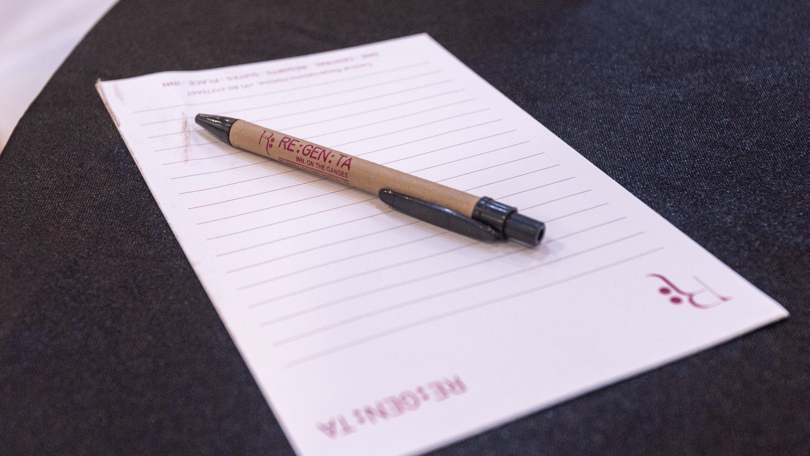 A paper and a pen on a black surface with DLS Hotels On The Ganges logo.