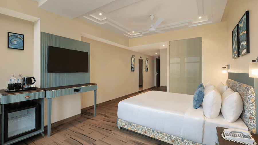 A room with a large bed, spreads, pillows, a television, and windows that is one of the hotel rooms in Nagpur at Essentia Luxury Hotel and Convention.