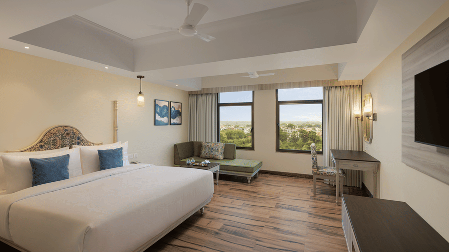 A room with a large bed, spreads, pillows, a television, and windows at Essentia Luxury Hotel and Convention, a 5-star hotel in Nagpur.