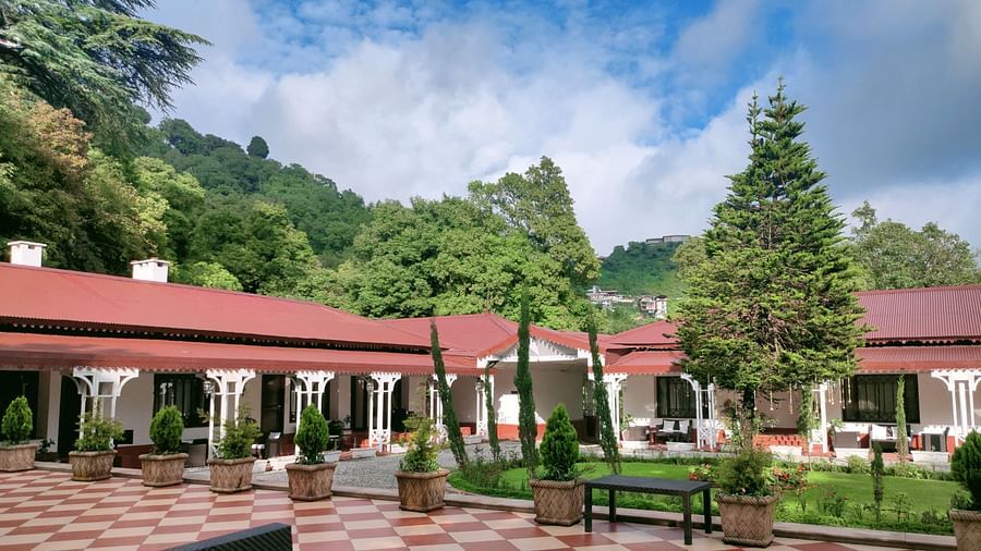 Facade view of The Claridges Nabha Residence in Mussoorie with a backdrop of a lush green forest with a blue sky with clouds