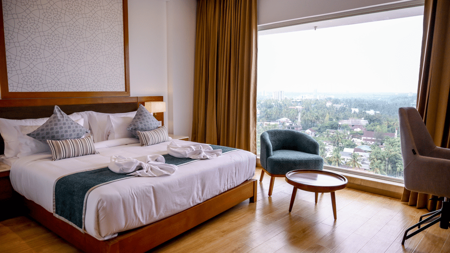 A hotel bedroom featuring a king size bed, a small coffee table with an armchair, and a large window overlooking trees at Tiara by MPS.