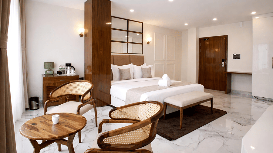 A Premium Triple Room at Valmere Chery Blossom Suites featuring wooden chairs with woven backs, a small round table, and a bed with a plush headboard.