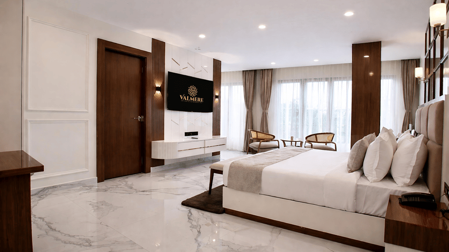 A Premium Triple Room at Valmere Chery Blossom Suites featuring a large bed, wall-mounted TV, marble flooring, and seating area by floor-to-ceiling windows.