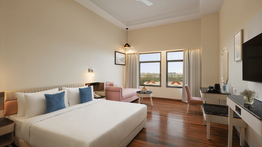 A room with a large bed, a sofa, a table spreads, pillows, a television, and windows at Essentia Luxury Hotel and Convention, Nagpur