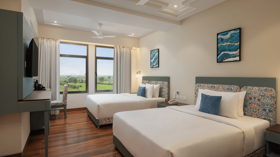 A room with a twin beds, spreads, pillows, a television, and windows at Essentia Luxury Hotel and Convention, Nagpur