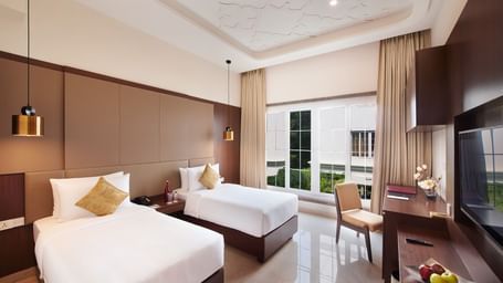 An image of a bedroom featuring two similar looking beds, a work desk and chair, and a flat TV screen - Accord Metropolitan