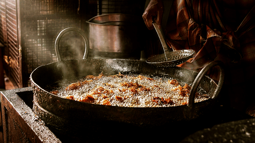 a large vessel with items being fried by a street vendor with the ray of sun shine hitting on the side
