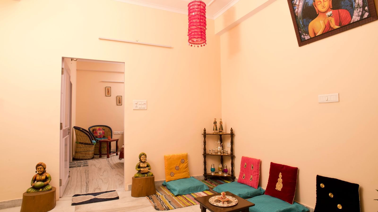 A seating area with floor cushions, low table, wall hanging, and framed picture above in a room at Jaypore360 Homestay in Jaipur.