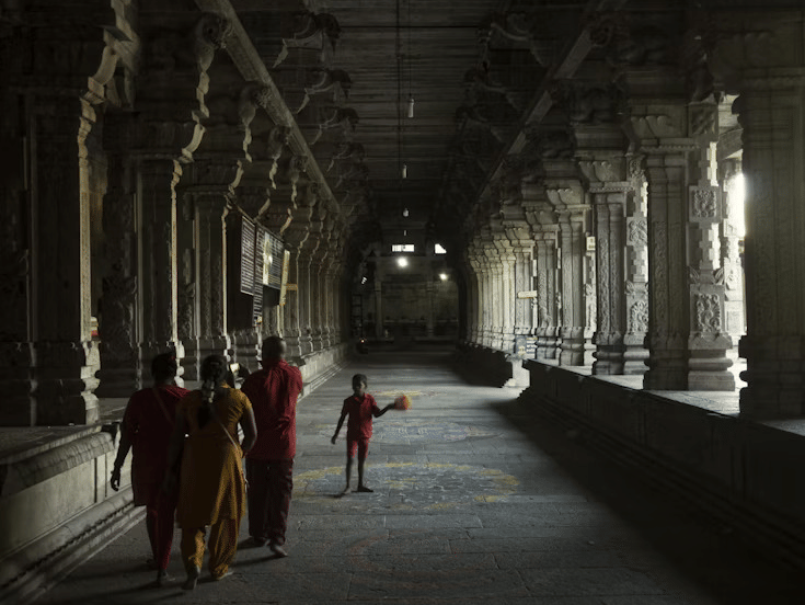 Dimly lit temple corridor with carved stone pillars and a group of people walking, capturing a serene and historic atmosphere.