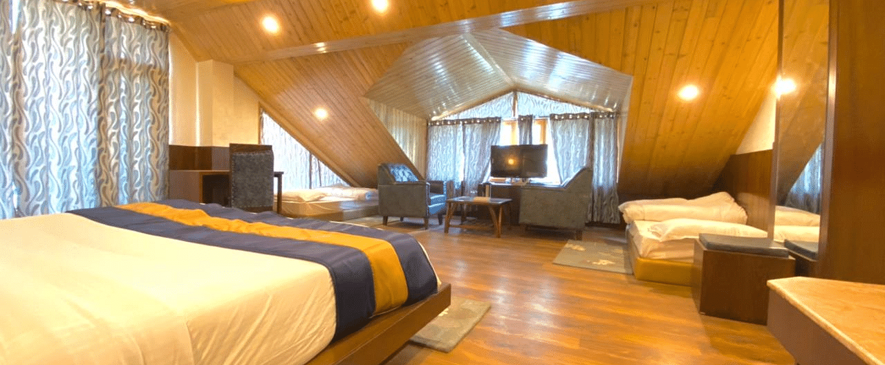 A spacious, well-lit room at La Serene Valley, Manali, with wood-paneled interiors, a large bed, a sitting area, and two single beds.