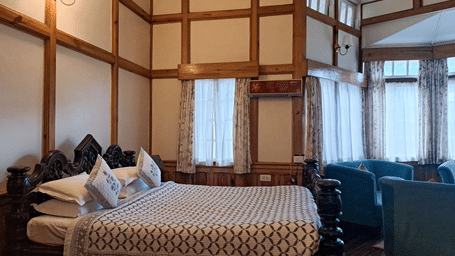 A room at The Heritage Club, featuring a large bed, spreads, pillows, windows, and a wall lamp.