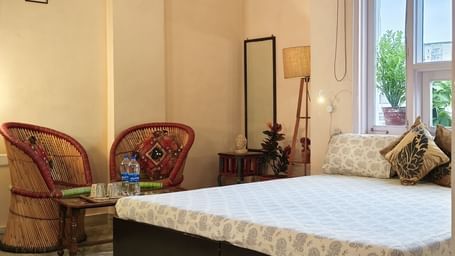 Bedroom with double bed, two chairs, table, lamp, and mirror near window at Jaypore360 Homestay in Jaipur
