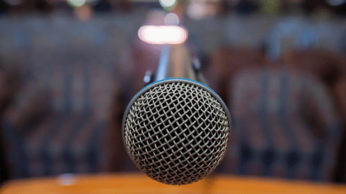 A close up view of a mic with empty chairs blurred in the background.