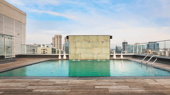 Rooftop swimming pool with clear blue water and a city skyline view under a bright sky.