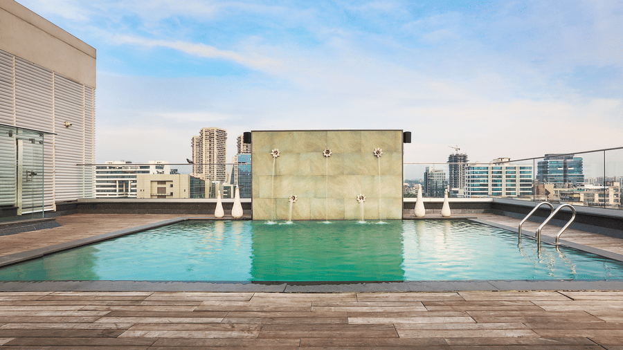 Rooftop swimming pool with clear blue water and a city skyline view under a bright sky.