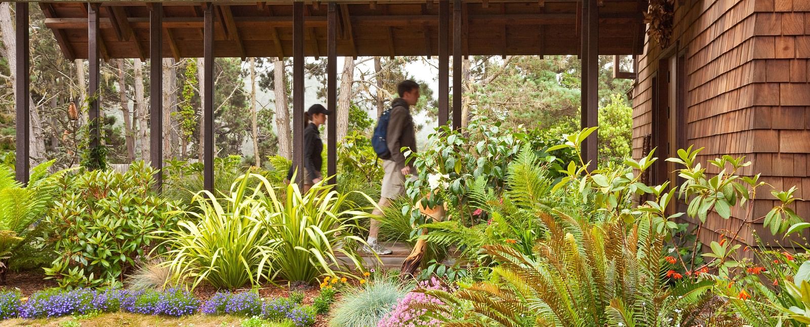 A shaded outdoor patio with lush landscaping with guests walking behind it - Brewery Gulch Inn & Spa