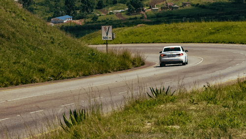 A car driving on a hilly road surrounded by green slopes.