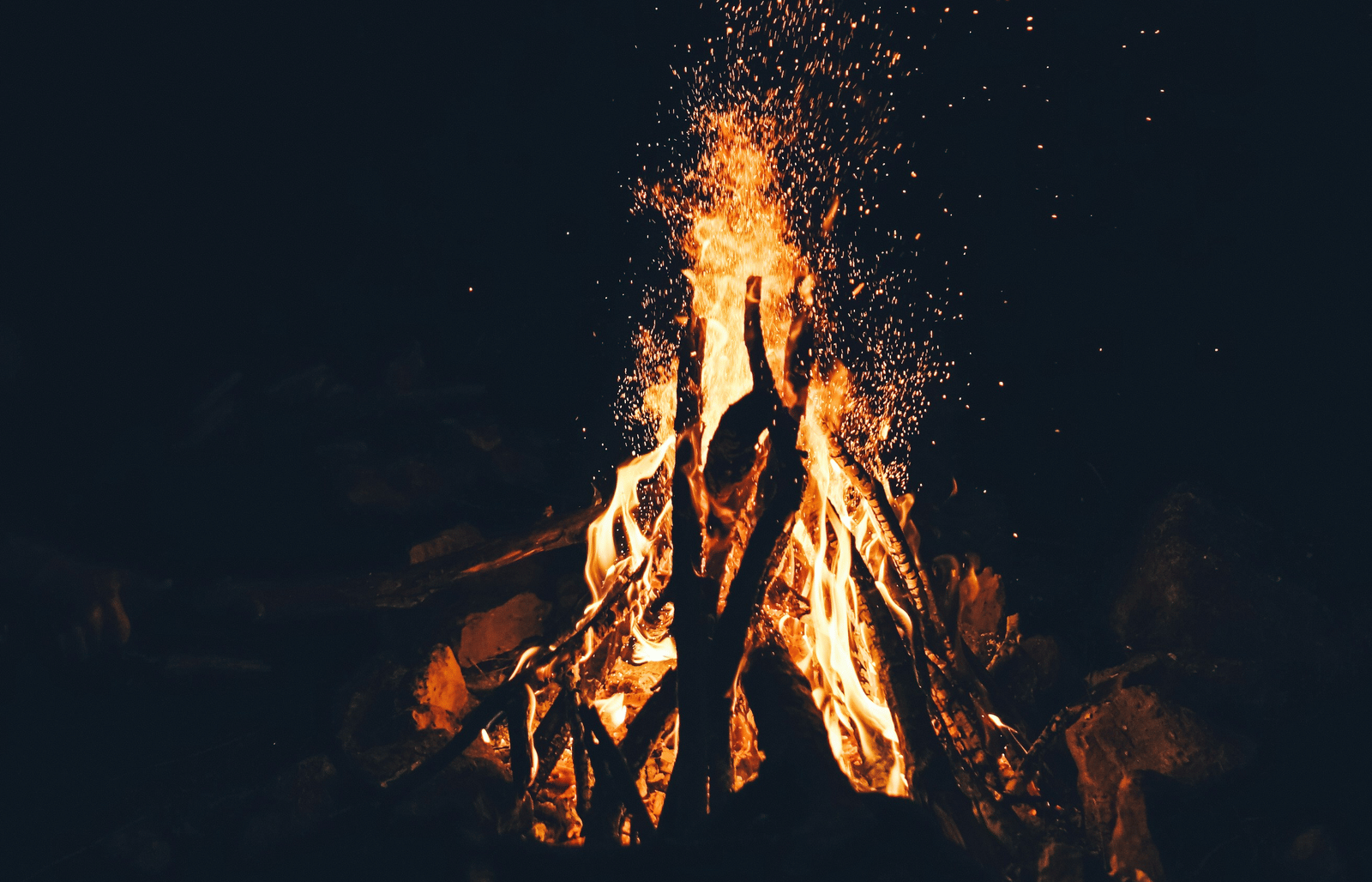 A bright bonfire burning in the darkness with sparks rising into the night air.