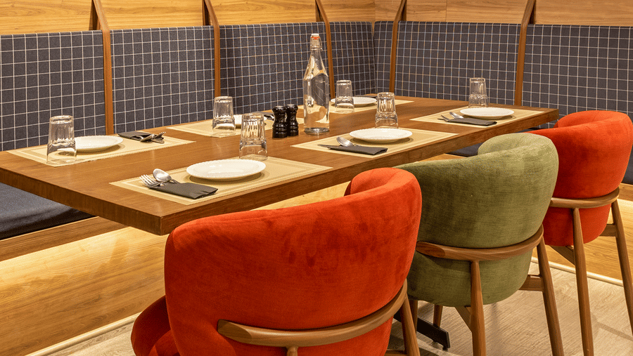 A set dining table with chairs inside Koi Garden. Cutlery and glasses are positioned on the table surface. A light fixture hangs from the ceiling above the seating arrangement.
