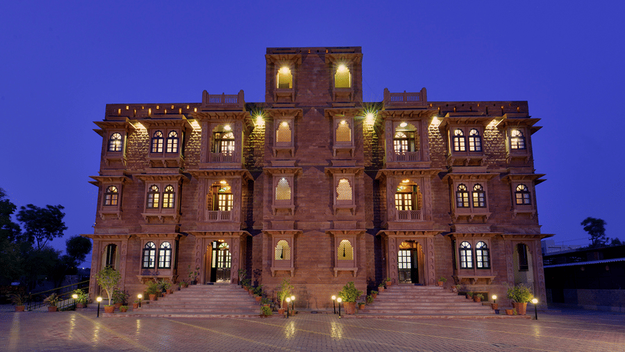 A large stone facade of Garh Govind featuring lit windows and entryways against a dark blue twilight sky.