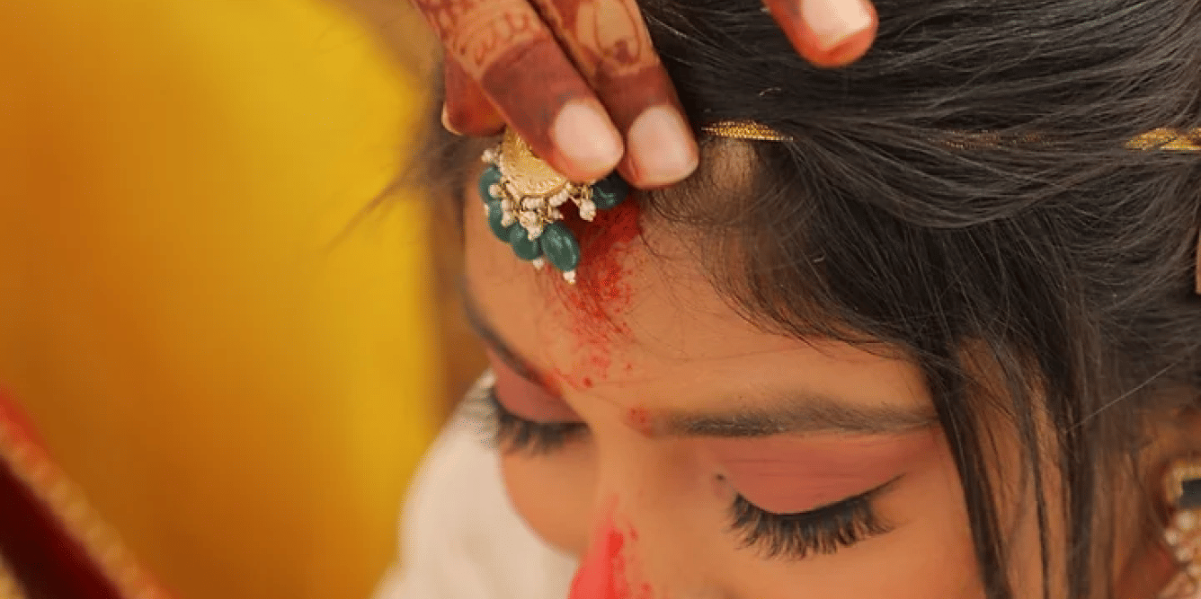 Image of a woman having her maang tikka adjusted.