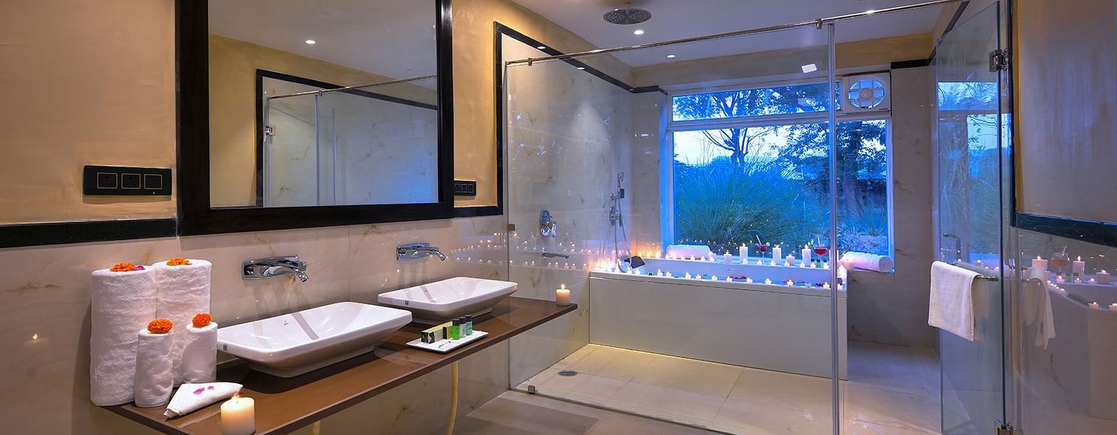 Luxury Suite Cottage with a double vanity, large mirror, glass shower enclosure, candlelit bathtub by a window, and recessed lighting in a bathroom - Singhvilas, Ranthambore