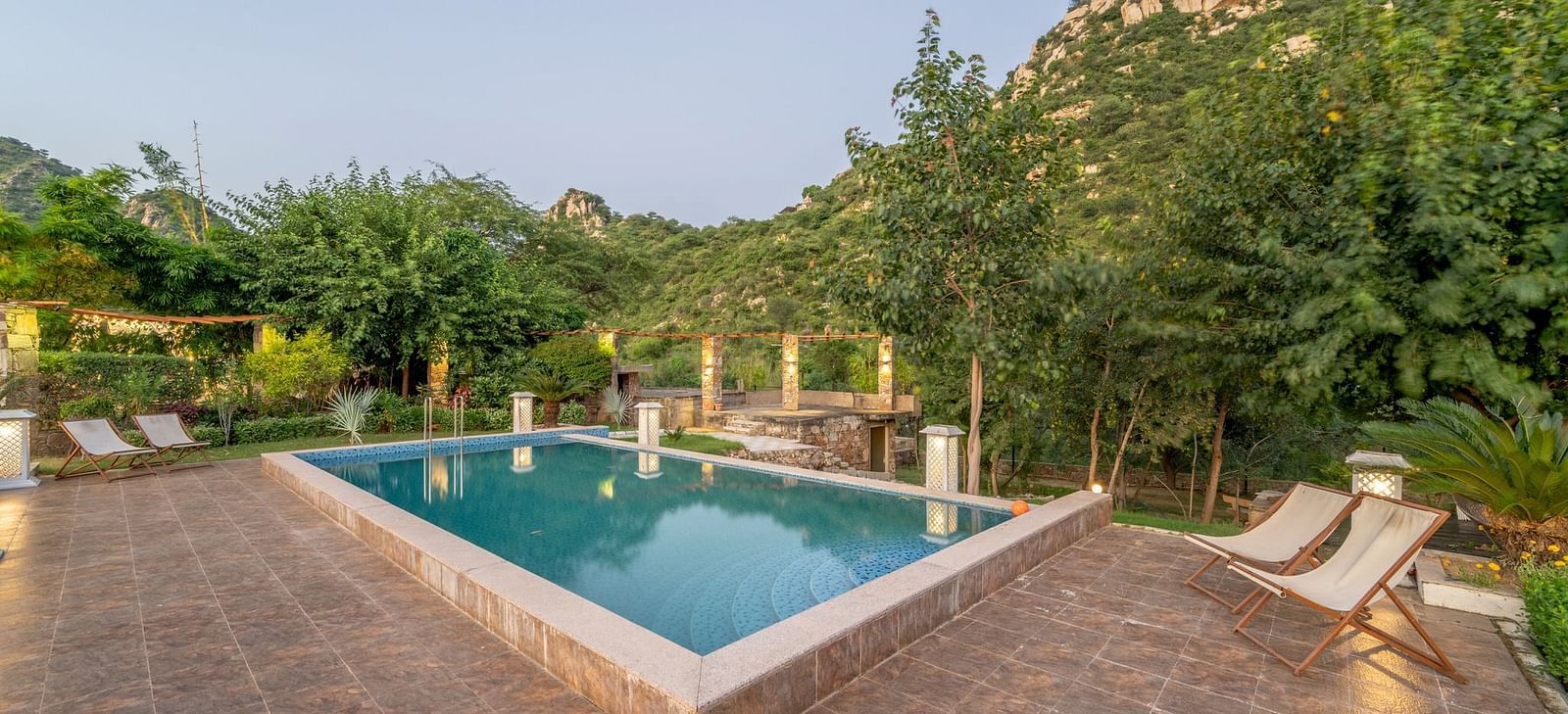 An outdoor pool at Valley by Grassfield, surrounded by plants and trees, with two lounge chairs on the side.