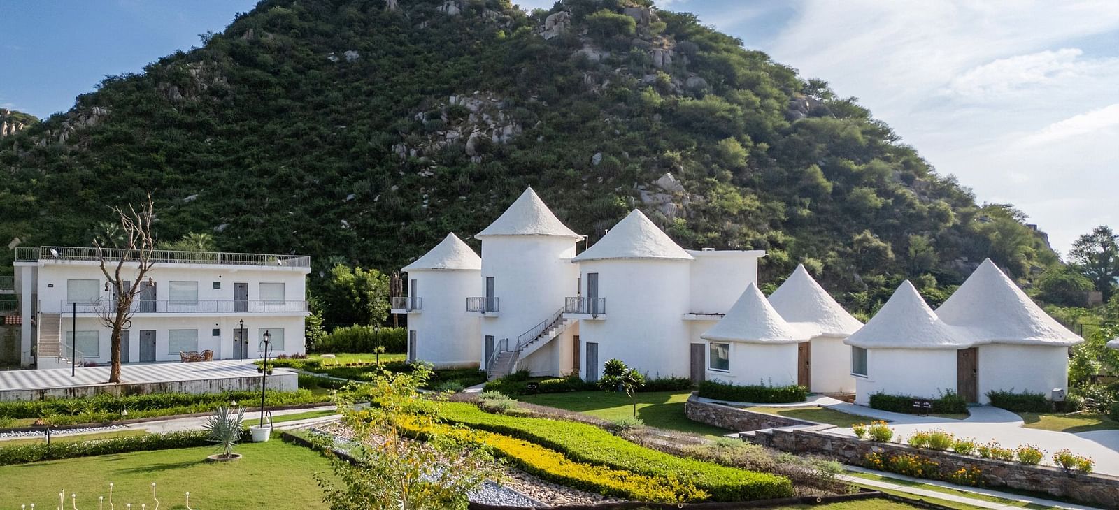 Conical-roof accommodations with an open space in front, set against a scenic mountain backdrop at Valley by Grassfield.