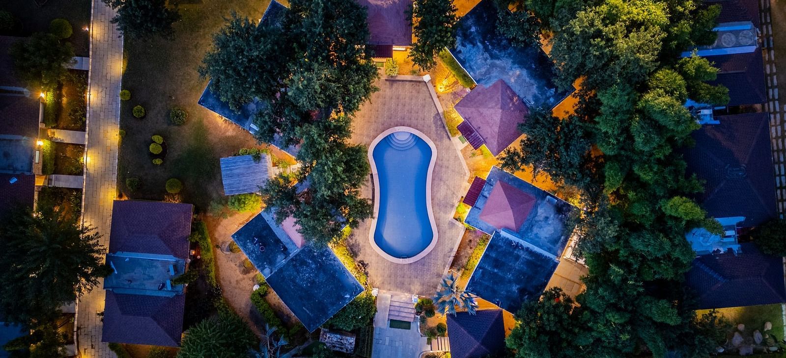 Aerial view of Valley by Grassfield, highlighting the accommodations illuminated by glowing lights, with a swimming pool at the centre.