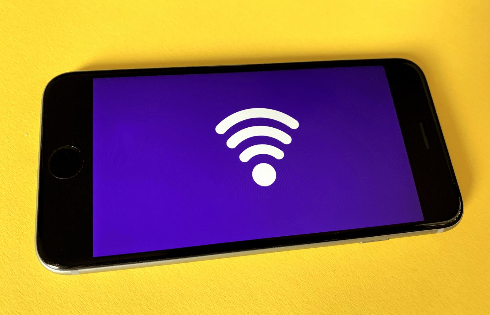 A mobile phone on a yellow table with wi-fi signal logo on the phone