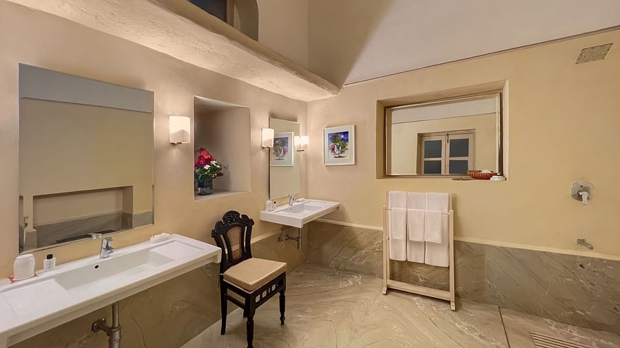 A bathroom with two sinks, two mirrors, a chair, and a towel rack at Tijara Fort-Palace - 19th Century, Alwar.