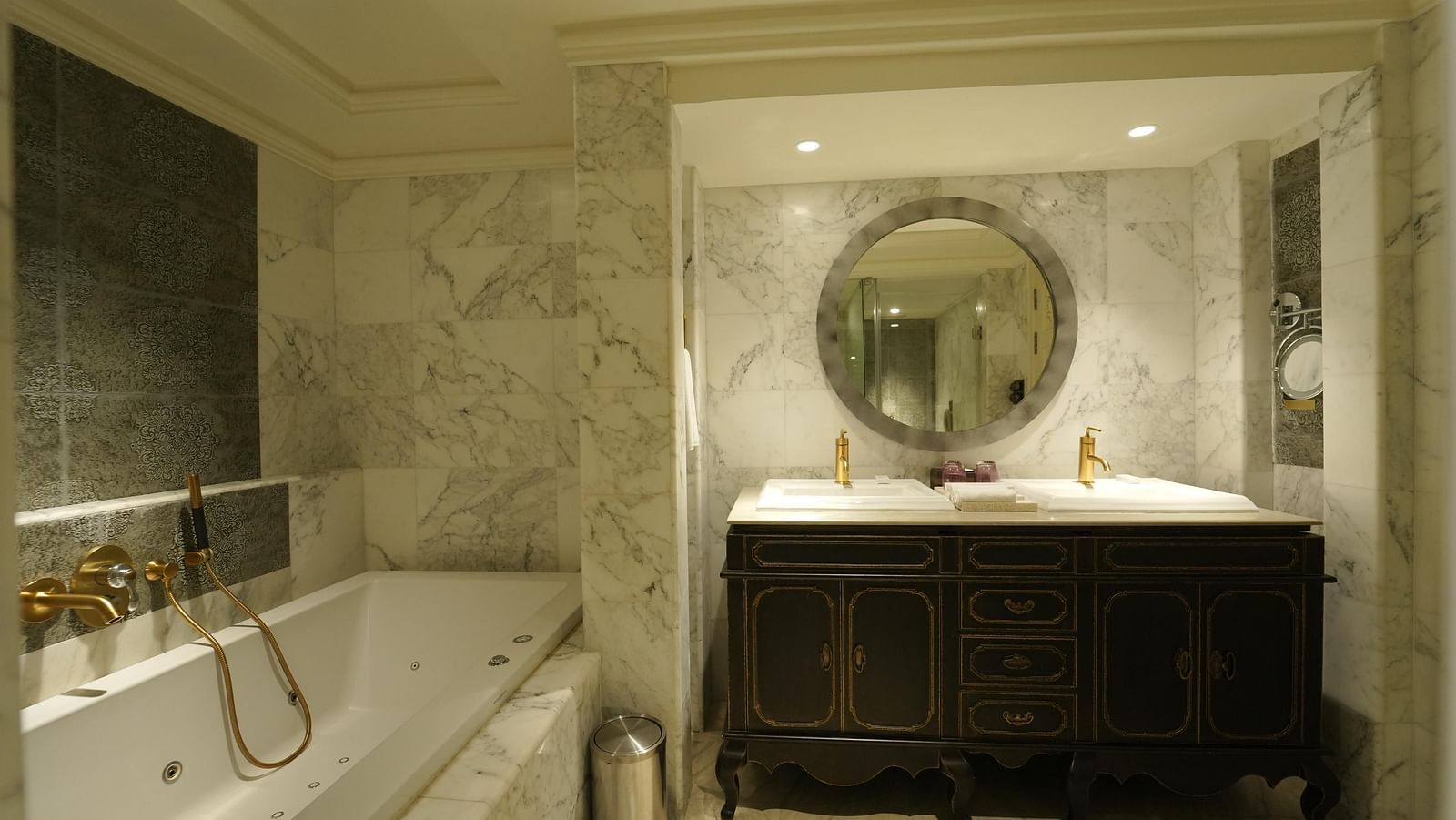 A bathroom at Fragrant Nature Cochin with a Jacuzzi tub, twin sinks, dustbin, mirror and elegant marble interiors.