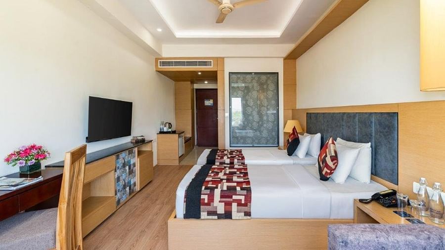Standard Twin Room with twin beds, large window, TV, and seating area at Golden Tulip, Udaipur.