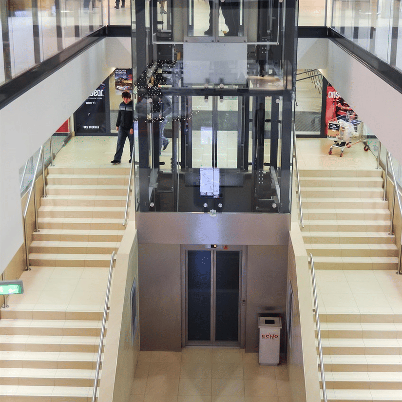 A mall interior showing escalators, stairs, bright lighting, and multiple floors with glass railings and open walkways.