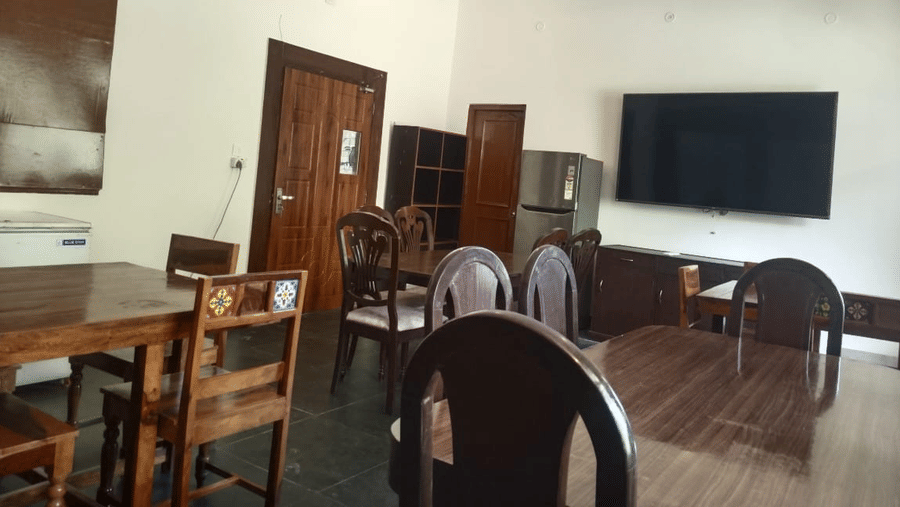 Indoor dining area with wooden tables and chairs, a wall mounted television and ceiling fan.