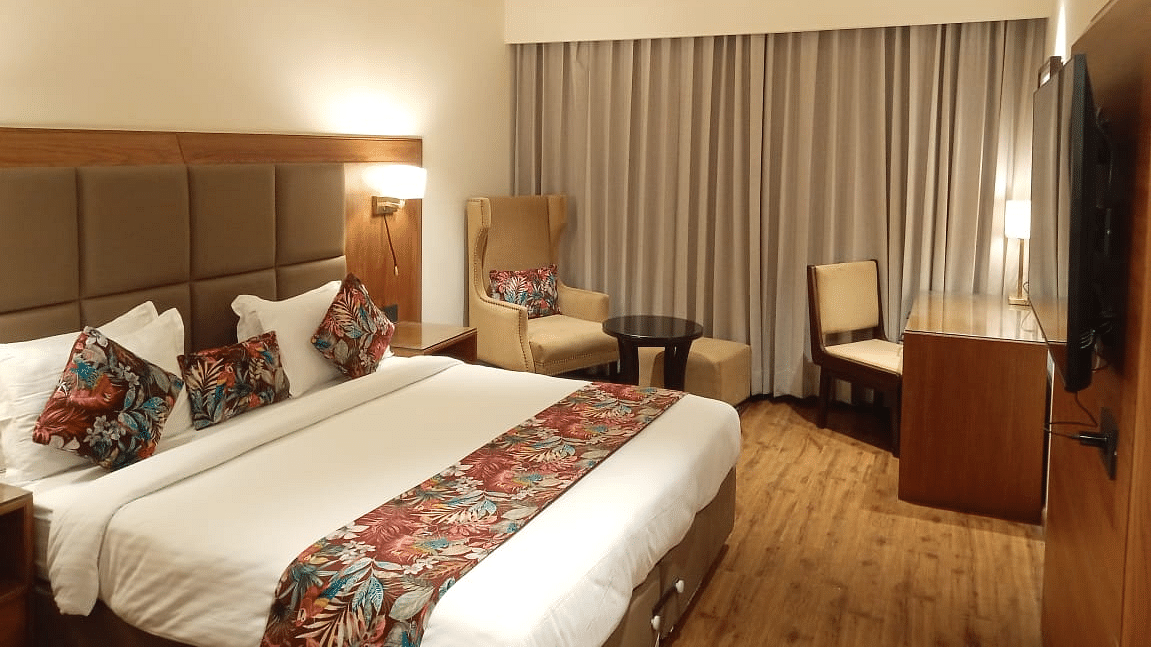 Modern hotel room with a king size bed, floral accents, a seating area with an armchair and table, a work desk, and a wall-mounted TV - Clarks Inn Express, Ludhiana