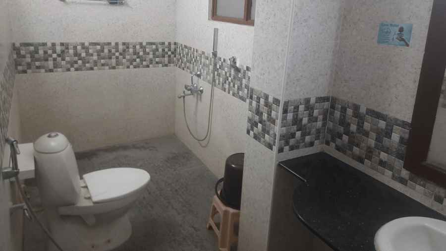 Bathroom at Udipi Home, Egmore, Chennai featuring a wall-mounted toilet, handheld shower, and patterned wall tiles.