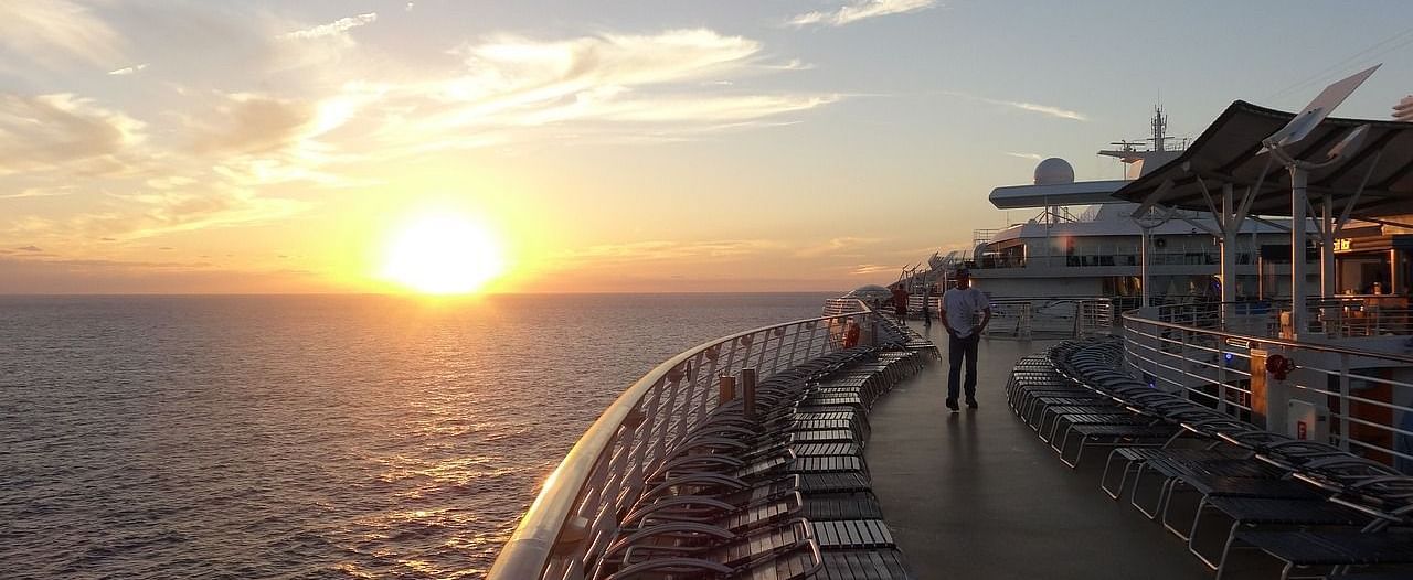 A beautiful sunset scene with the sun sinking into the ocean, viewed from the deck of a ship with lounge chairs in the foreground.