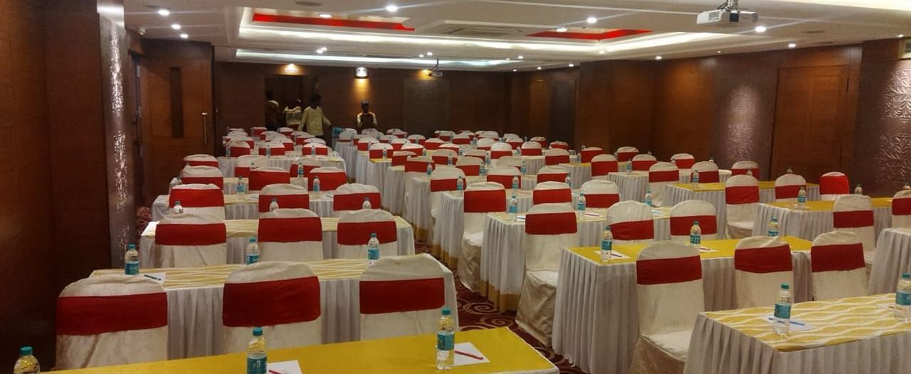 A conference hall set up with rows of tables and chairs, ready for attendees- The President Hotel Jayanagar, Bangalore