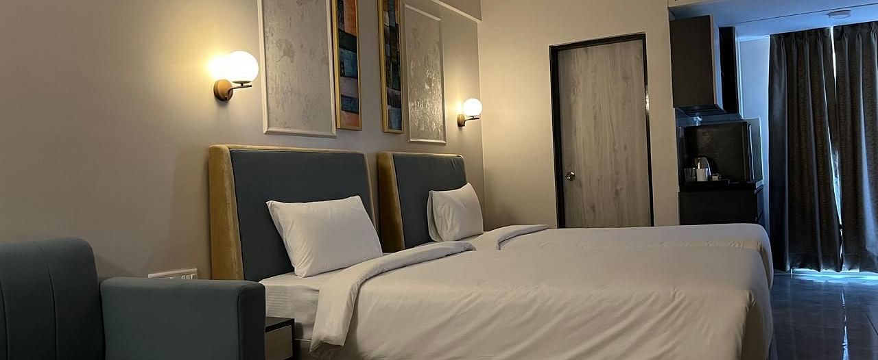 A side view of the spacious room featuring twin beds, a wall-mounted night lamp, and a photo frame above the headboard at Urban Suites by BluSalzz, Jaipur.