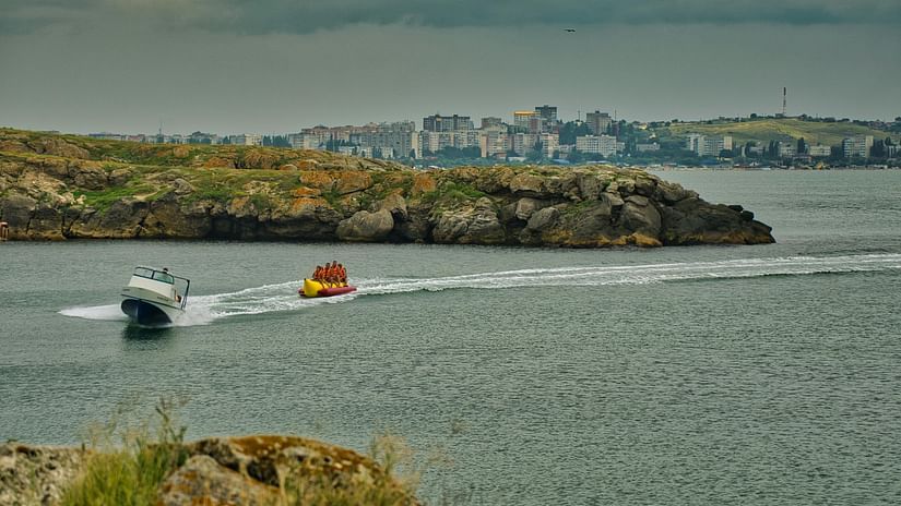 A speedboat towing people on a banana boat near the shore