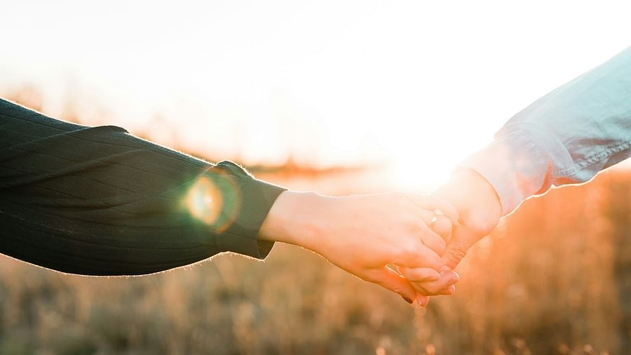Two persons holding hands, during the golden hour, while walking through a field.