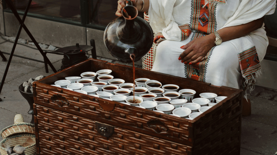 A woman in traditional Ethiopian attire pouring coffee from Jebena into cups.