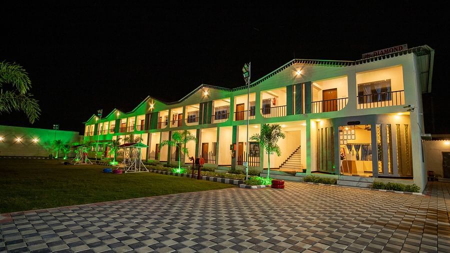 A close-up view of the resort building at night, beautifully lit in green with landscaped surroundings - VITS Select Diamond Resort, Sasan Gir