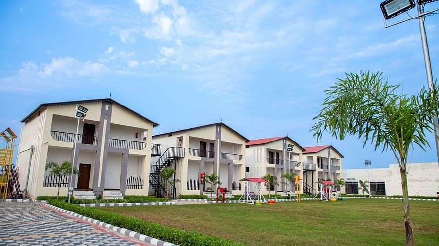 A view of the resort with a paved pathway leading towards the buildings, surrounded by green lawns and palm trees - VITS Select Diamond Resort, Sasan Gir