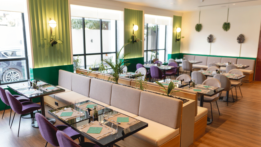 Bright, modern Meli-Melo restaurant interior with accents, large windows, potted plants, and neatly set tables with chairs and beige booth seating.