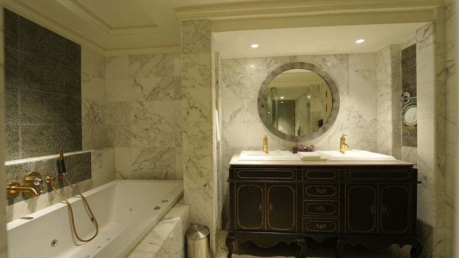 A bathroom at Fragrant Nature Cochin with a Jacuzzi tub, twin sinks, dustbin, mirror and elegant marble interiors.