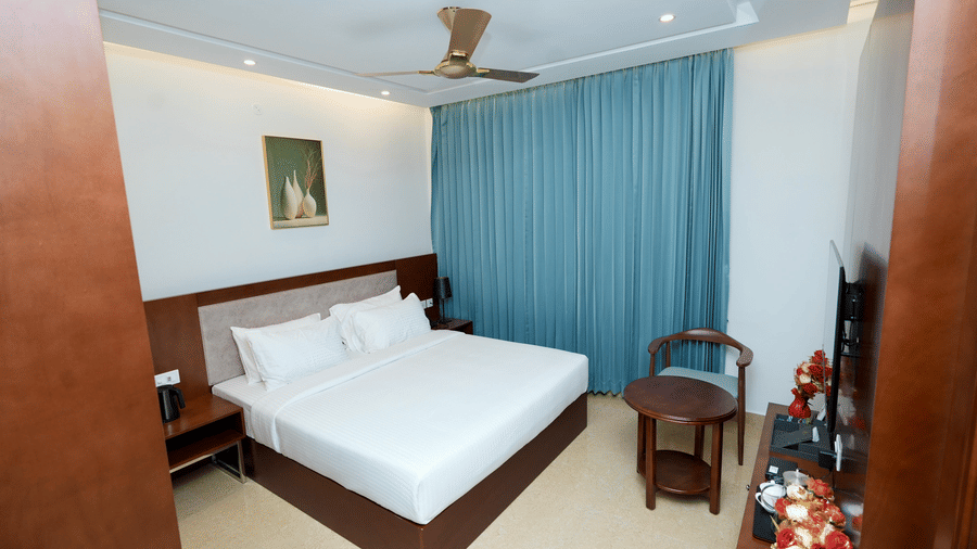 A side view of Deluxe King Room  in Le Royale Palace with a double bed, a large window with draped curtains, and wooden interiors