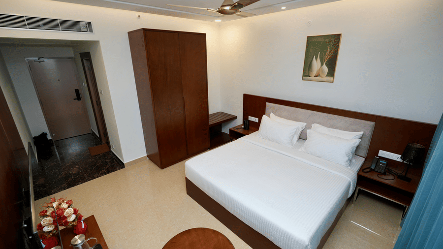 The Deluxe Kind Room of Le Royale Palace showcasing a double bed, 2 side tables, a large wooden cabinet, glowing ceiling lights, round coffee table, and a flat-screen TV mounted on the wall 
